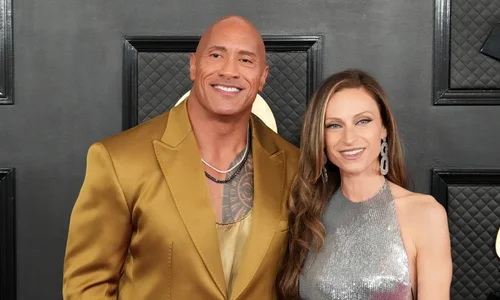 Dwayne "The Rock" Johnson in a gold suit poses with wife Lauren Hashian in a silver dress on a red carpet.