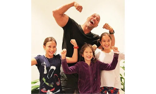 Dwayne "The Rock" Johnson and three young girls smiling together while holding a playful, matching pose for a photo.