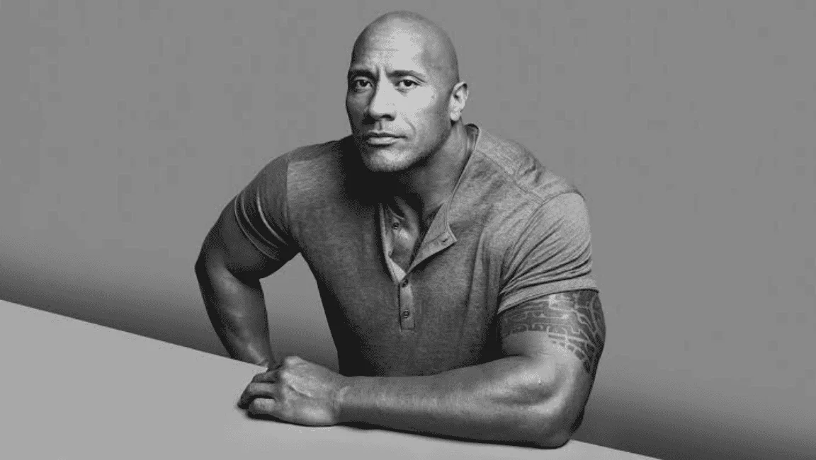 Black and white portrait of Dwayne "The Rock" Johnson in a henley shirt leaning forward.
