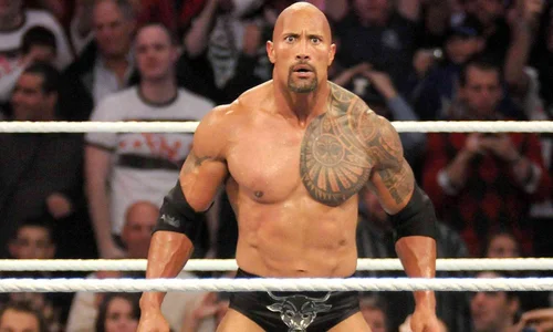 Dwayne "The Rock" Johnson stands in a WWE ring wearing black trunks with his signature Brahma Bull logo.