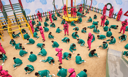 Squid Game honeycomb challenge - players cutting shapes (circle, triangle, star) with guards watching