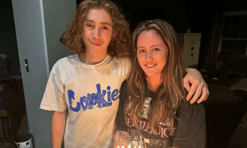 Jace and his mom Jenelle smile together while holding a birthday cake with lit candles.