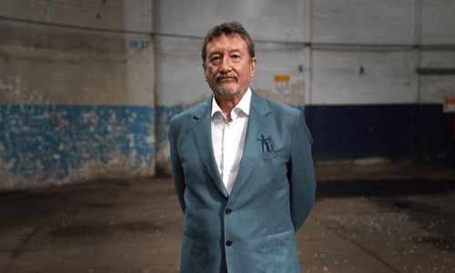 Steven Knight in a blue suit standing in a warehouse.