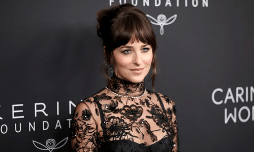 Dakota Johnson wearing a see-through Gucci lace gown with emerald jewelry on the red carpet in NYC.