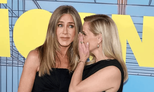 Jennifer Aniston and Reese Witherspoon share a playful whisper on the red carpet at a premiere event.