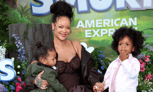 Rihanna smiles, holding her youngest son. Her older son stands beside her, holding her hand, at a movie premiere.