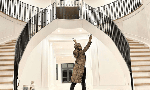 A woman in a black sequin gown posing at a red-carpet style event against a dark backdrop.