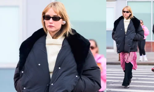 Jennifer Lawrence walks outside wearing a black puffer coat, sunglasses, and a pink scarf wrapped over black pants.