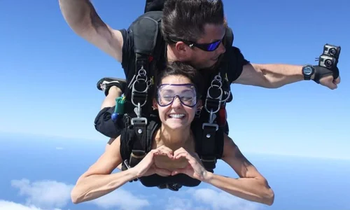 Nina Dobrev smiling in skydiving gear while mid-air during an extreme sports adventure.