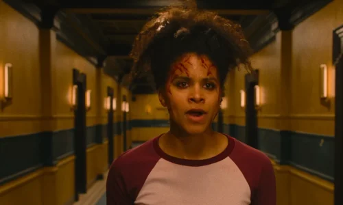 A movie still from 'They Will Kill You' featuring Zazie Beetz with blood on her face standing in a dim hallway.