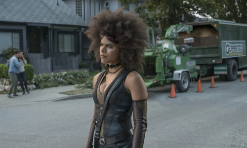 Zazie Beetz as Domino in Deadpool 2, standing on a residential street in her black and gold tactical suit.