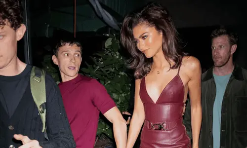 Zendaya in a burgundy leather midi dress holding hands with Tom Holland as they navigate through a crowd during a night out.