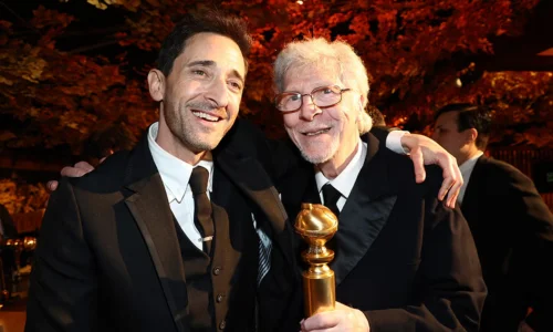 Adrien Brody smiling during a red carpet press interview event.