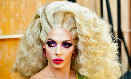 Alyssa Edwards from RuPaul's Drag Race with voluminous blonde hair, purple eye shadow, and pink lipstick in a side-profile view.