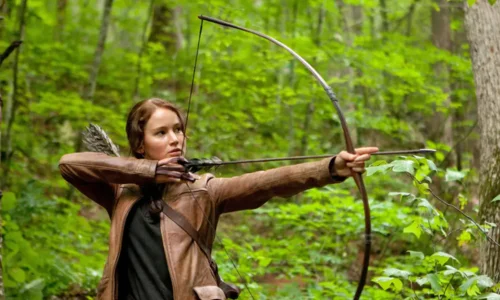 Jennifer Lawrence as Katniss Everdeen holding a bow and arrow in a scene from The Hunger Games.