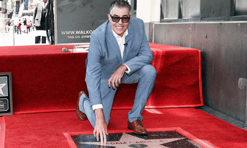 Comedian Adam Carolla posing next to his new star on the Hollywood Walk of Fame.