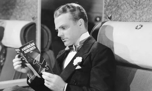 James Cagney reading a magazine while seated on an airplane in a classic black-and-white photo