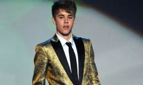 Young Justin Bieber smiling wearing a textured metallic gold blazer over a white collared shirt and a black tie.