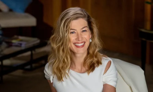Rosamund Pike smiling during an indoor portrait session while wearing a white dress