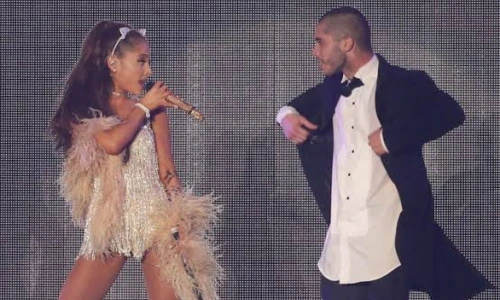 Ariana Grande in a sparkly fringe dress performing on stage alongside a male backup dancer.