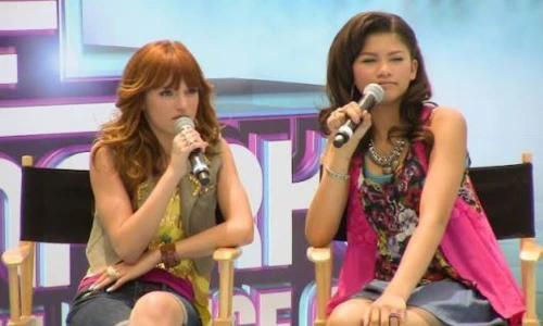 Bella Thorne and Zendaya sit in director's chairs, holding microphones at a Disney Channel Shake It Up event.
