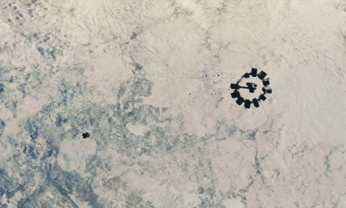 High-angle aerial view of the Endurance spacecraft from the movie Interstellar orbiting over a vast, frozen planet covered in white ice, snow, and textured glacial formations.
