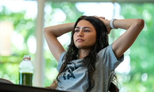 Zendaya leans back with hands behind her head in a grey t-shirt in a scene from Challengers.