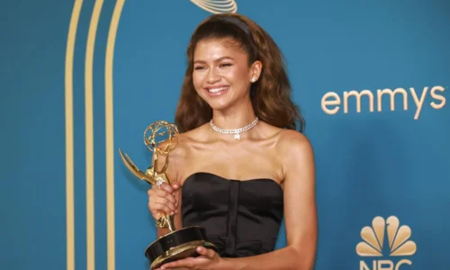 Zendaya smiles brightly while holding a gold Emmy Award trophy against a blue background featuring the Emmys and NBC logos.