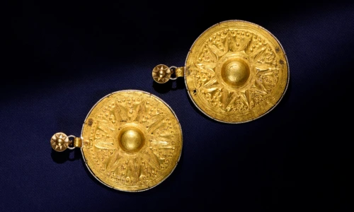 Ancient circular gold earrings with a sunburst design and star studs against dark blue fabric.
