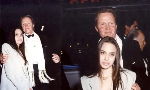 Angelina Jolie smiles alongside father Jon Voight at a formal event, wearing an oversized grey suit and pearl necklace.