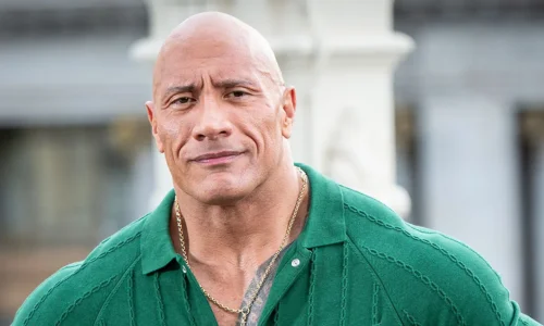 Close-up portrait of a smiling Dwayne "The Rock" Johnson wearing a green knit polo shirt and a gold chain necklace.