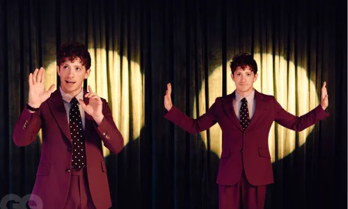 Ethan Slater standing in a burgundy suit in front of a stage curtain