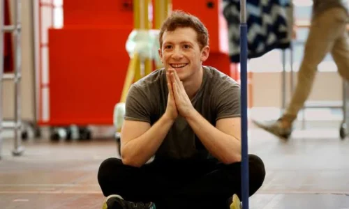 Ethan Slater sitting cross-legged on a rehearsal room floor