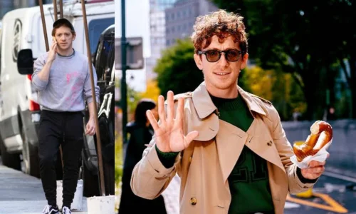 Ethan Slater waving while holding a bagel on a city street