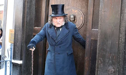 Johnny Depp as Ebenezer Scrooge standing outside a Victorian building in costume