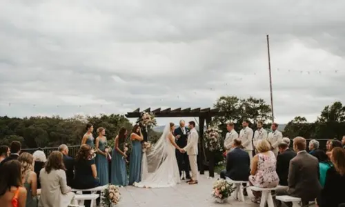 A bride and groom exchange vows under a wooden pergola during an outdoor patio wedding ceremony.