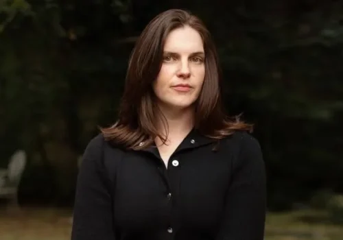 Film editor Jennifer Lame posing outdoors in a black button-down cardigan with blurred trees in the background.