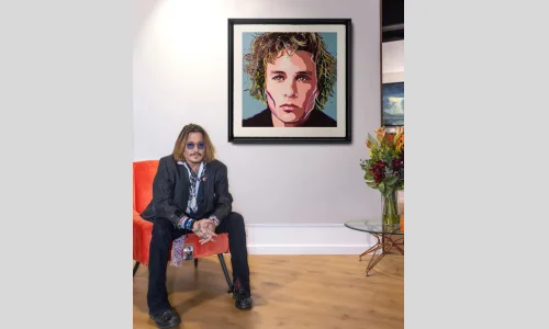 Man wearing blue sunglasses sitting beside a framed colorful portrait artwork in an art gallery