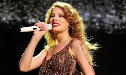 Taylor Swift performing live on stage in a sparkly gold fringe dress while holding a microphone.
