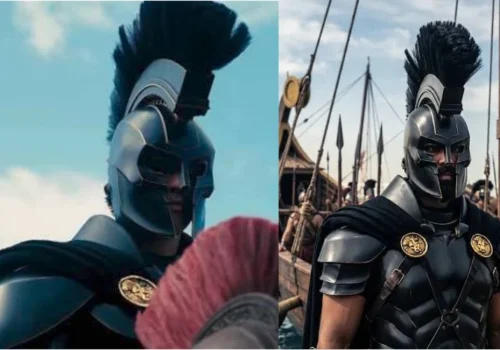 Warrior wearing black armor and a tall crested helmet standing beside a ship with soldiers in the background.