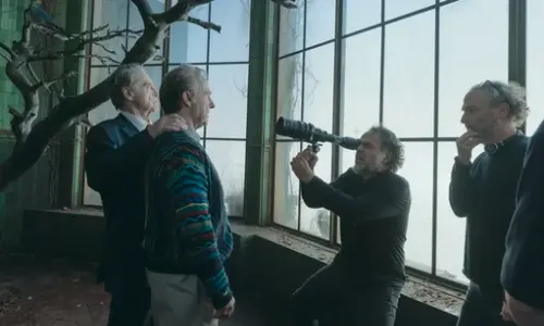 Director Alejandro Iñárritu looks through a camera viewfinder on set while directing actors in a green room.