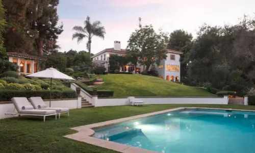 Swimming pool surrounded by landscaped gardens, lounge chairs and tall trees