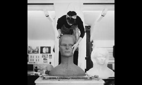 Black and white photo of artist Prune Nourry sculpting a large clay bust in her studio for the Petit Palais show.