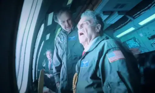 Tom Cruise as Digger Rockwell wearing heavy aging makeup and a green flight suit in a film still.