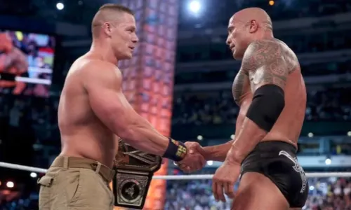 John Cena and Dwayne "The Rock" Johnson shake hands in a WWE ring as Cena holds the championship belt.