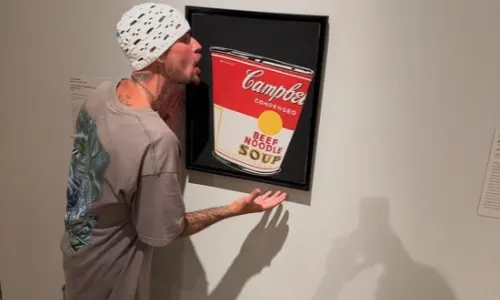 Justin Bieber pretends to sip from a framed painting of Andy Warhol's Campbell's Soup Can in a gallery.