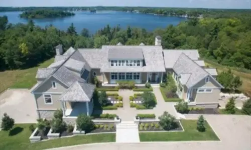 Lakefront mansion with a large driveway, landscaped gardens and trees surrounding the property