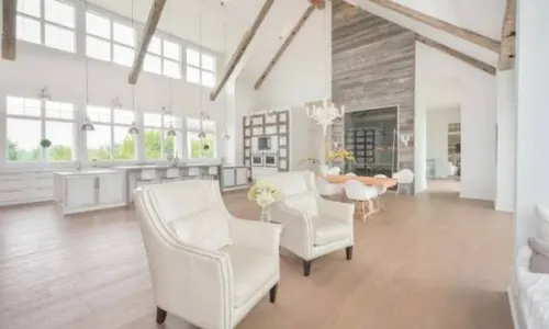 Bright mansion living room with high ceilings, exposed wooden beams, large windows and white armchairs
