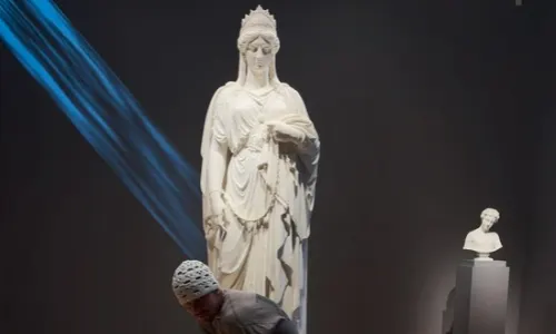 Justin Bieber leans in close to view the marble sculpture "Zenobia in Chains" under blue gallery lighting.